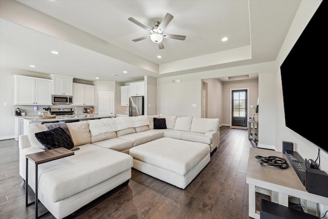 living room featuring a tray ceiling, recessed lighting, dark wood finished floors, and baseboards