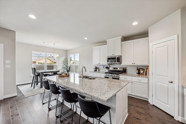 kitchen with dark wood-style flooring, a center island with sink, appliances with stainless steel finishes, white cabinetry, and a sink