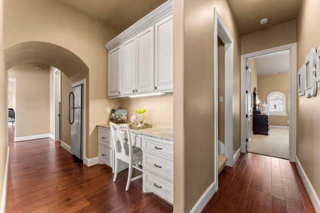 corridor featuring baseboards, arched walkways, and dark wood-type flooring