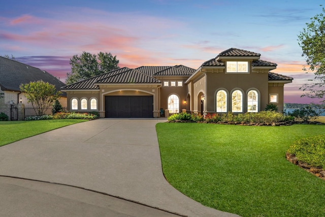 mediterranean / spanish house featuring a garage, a tiled roof, concrete driveway, stucco siding, and a front yard