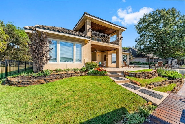 view of front facade with a patio, a balcony, fence, stucco siding, and a front yard