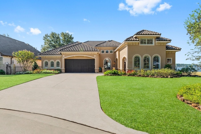 mediterranean / spanish-style house with a garage, driveway, a tile roof, a front lawn, and stucco siding