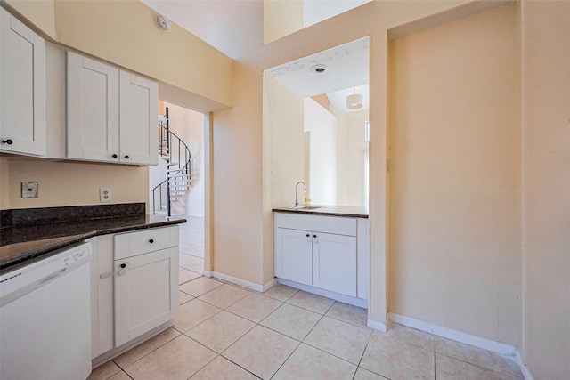 kitchen featuring a sink, dark stone counters, white cabinets, light tile patterned floors, and dishwasher