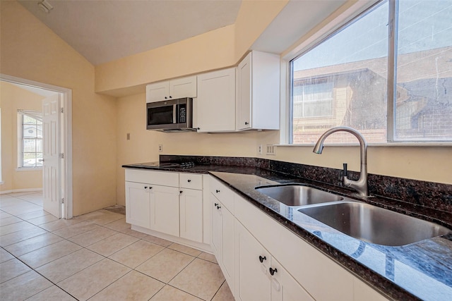 kitchen with stainless steel microwave, dark stone countertops, white cabinetry, and a sink