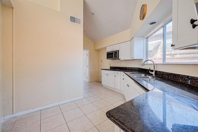 kitchen with dark stone countertops, light tile patterned floors, visible vents, a sink, and stainless steel microwave