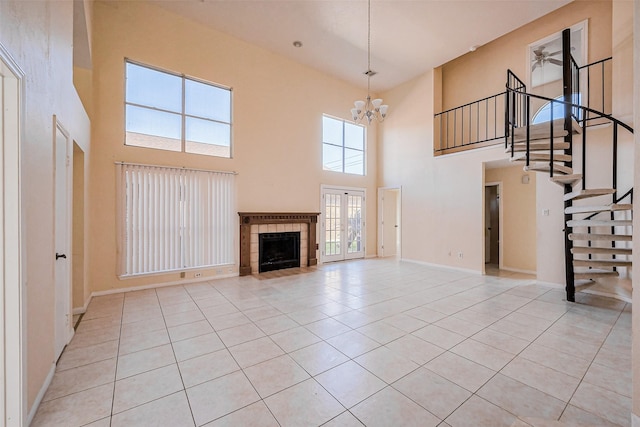 unfurnished living room with baseboards, a tiled fireplace, stairs, light tile patterned floors, and ceiling fan with notable chandelier