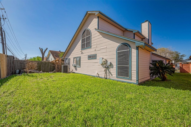 back of house with central air condition unit, a lawn, a fenced backyard, and a chimney