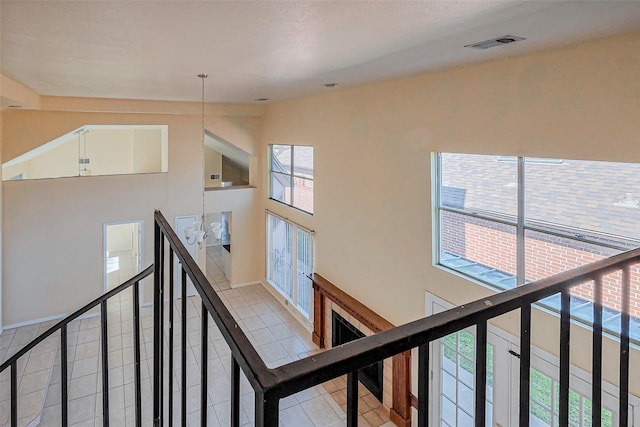 corridor featuring light tile patterned floors, visible vents, an upstairs landing, and lofted ceiling