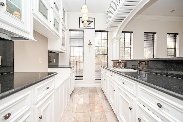 kitchen with glass insert cabinets, a sink, white cabinets, decorative light fixtures, and crown molding