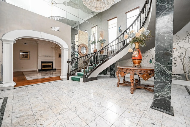 foyer entrance featuring arched walkways, marble finish floor, a fireplace, and a towering ceiling