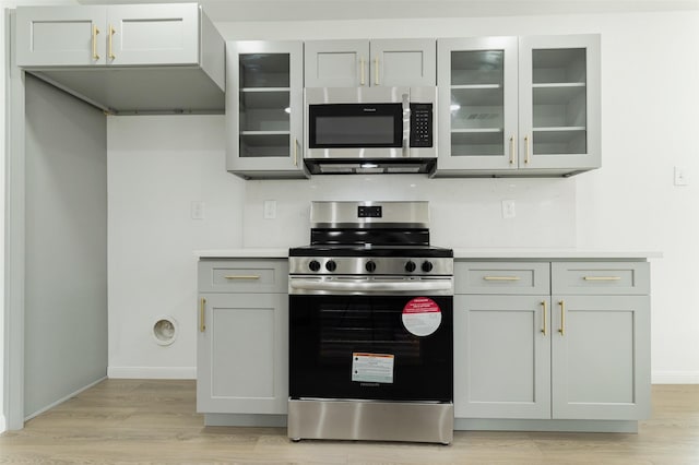 kitchen with light countertops, glass insert cabinets, gray cabinets, and appliances with stainless steel finishes