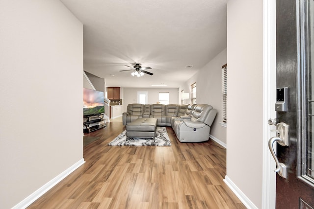 living area with light wood-style flooring, baseboards, and a ceiling fan