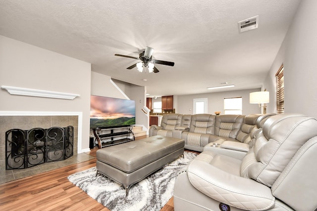 living area with a fireplace, visible vents, a ceiling fan, a textured ceiling, and wood finished floors