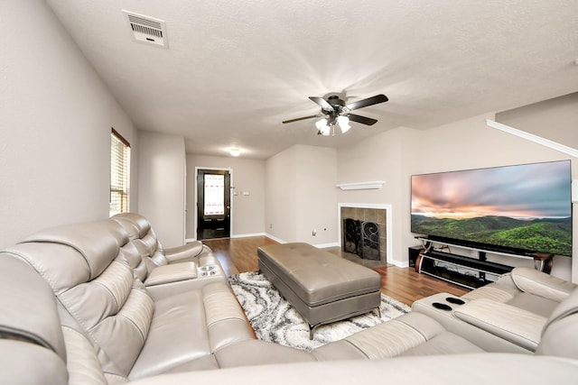 living area with ceiling fan, a fireplace, wood finished floors, visible vents, and baseboards