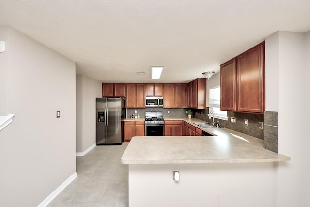 kitchen with stainless steel appliances, a peninsula, a sink, light countertops, and decorative backsplash