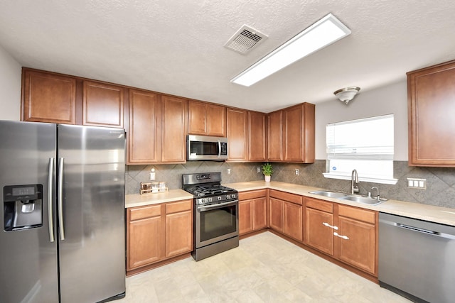 kitchen featuring brown cabinets, stainless steel appliances, light countertops, visible vents, and a sink