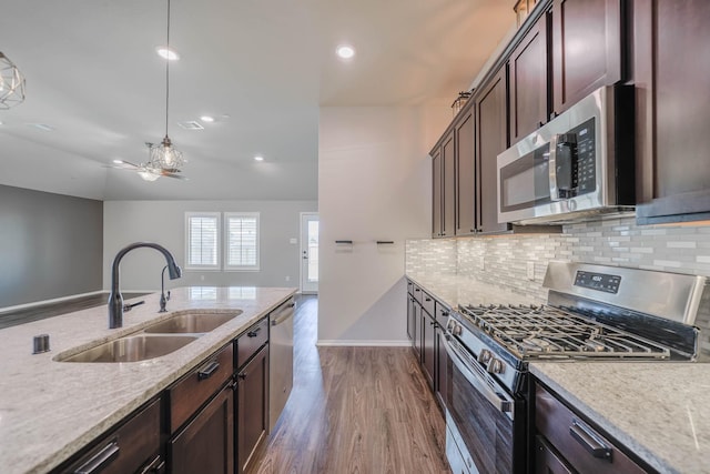 kitchen featuring dark wood-style floors, light stone counters, a sink, stainless steel appliances, and backsplash