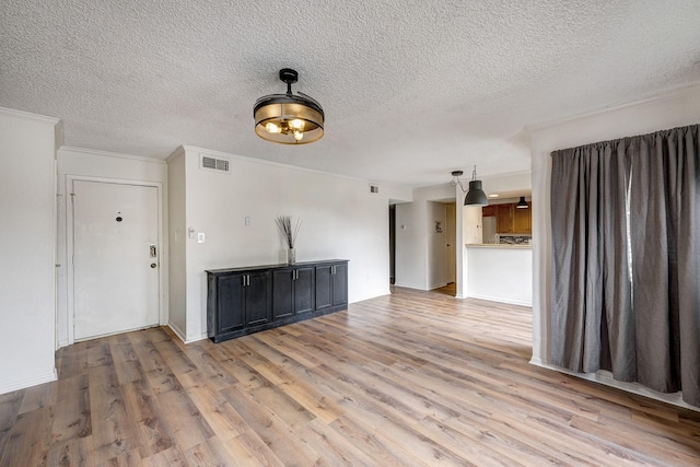 interior space featuring light wood-style floors, visible vents, ornamental molding, and a textured ceiling