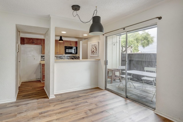 kitchen with brown cabinetry, light wood-style flooring, a textured ceiling, crown molding, and black microwave