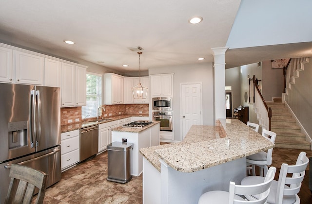 kitchen featuring a sink, white cabinets, appliances with stainless steel finishes, a center island, and tasteful backsplash