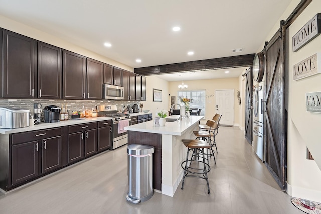 kitchen featuring stainless steel appliances, light countertops, decorative backsplash, a barn door, and a kitchen breakfast bar