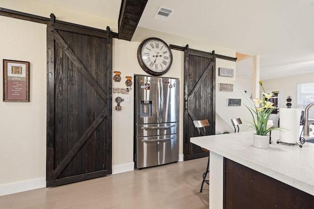 kitchen with a barn door, dark brown cabinetry, visible vents, a kitchen breakfast bar, and stainless steel fridge with ice dispenser