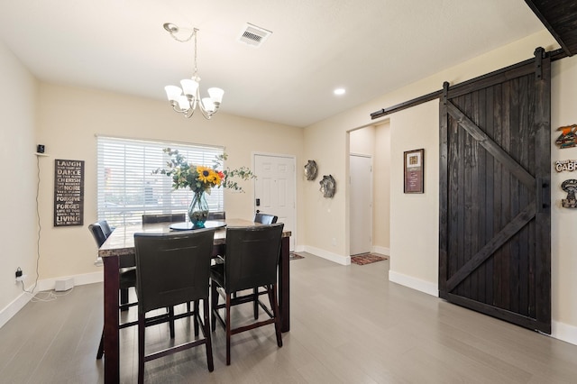 dining space featuring a barn door, baseboards, visible vents, wood finished floors, and a notable chandelier