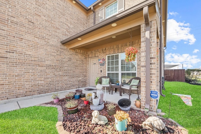 entrance to property featuring brick siding, a lawn, a patio area, and fence