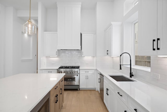 kitchen featuring white cabinets, appliances with stainless steel finishes, light stone counters, decorative light fixtures, and a sink