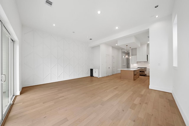 unfurnished living room featuring recessed lighting, visible vents, light wood-style floors, an accent wall, and baseboards