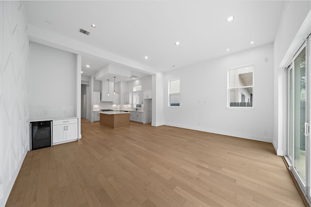 unfurnished living room featuring light wood finished floors, baseboards, visible vents, wine cooler, and recessed lighting