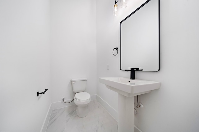 half bath featuring marble finish floor, toilet, and baseboards