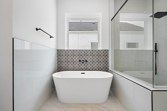 bathroom with marble finish floor, tile walls, a tile shower, and a freestanding bath