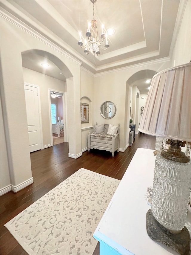 interior space with arched walkways, a raised ceiling, and dark wood finished floors