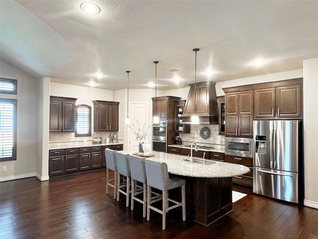 kitchen with dark brown cabinetry, dark wood finished floors, appliances with stainless steel finishes, custom exhaust hood, and a sink