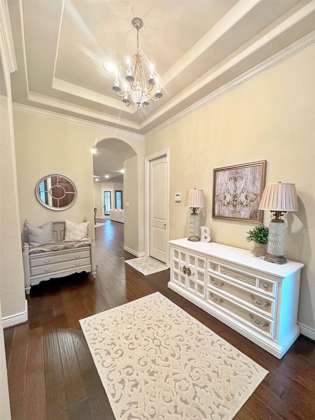 hall featuring arched walkways, dark wood-type flooring, a raised ceiling, and a notable chandelier