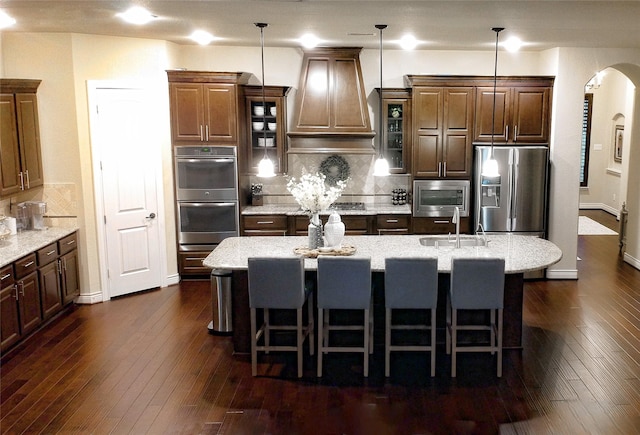 kitchen with arched walkways, dark wood finished floors, custom range hood, stainless steel appliances, and backsplash