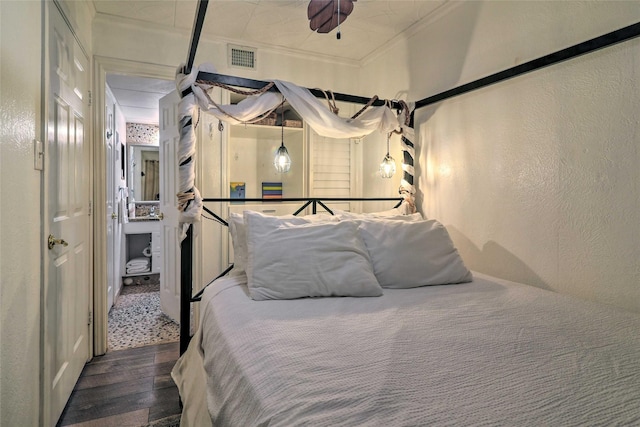 bedroom with a textured wall, visible vents, crown molding, and wood finished floors