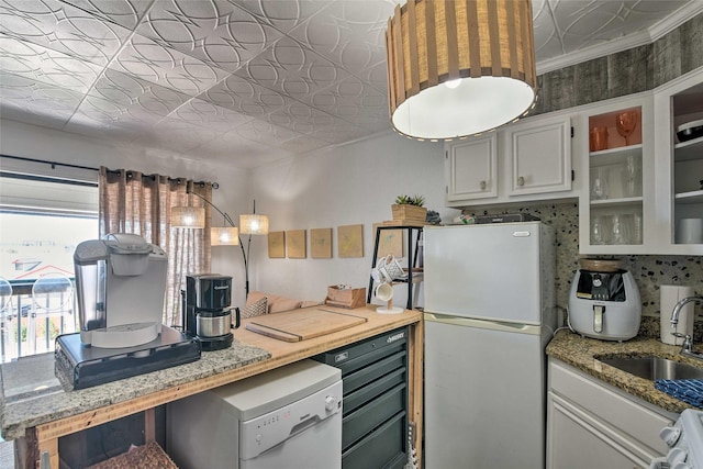 kitchen with light stone counters, a sink, backsplash, freestanding refrigerator, and an ornate ceiling