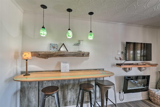 bar featuring baseboards, a glass covered fireplace, an ornate ceiling, wood finished floors, and crown molding