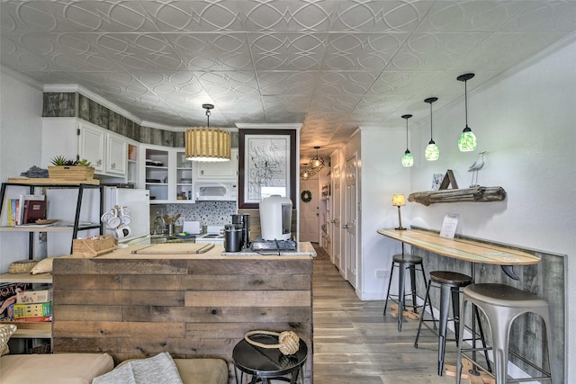 kitchen with an ornate ceiling, crown molding, open shelves, white microwave, and wood finished floors