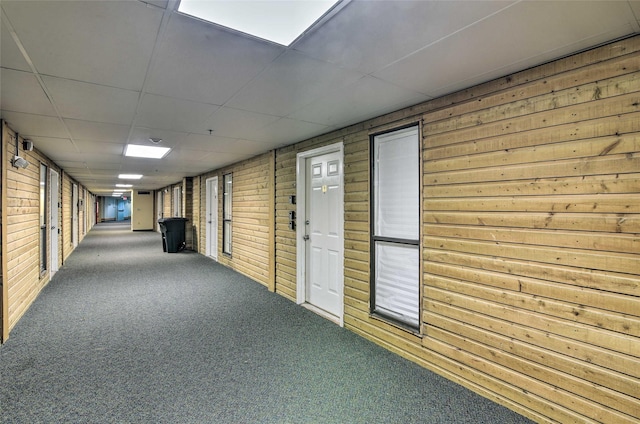 hall featuring a drop ceiling, carpet, and wooden walls