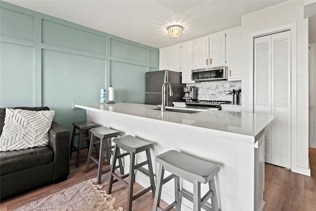 kitchen with a decorative wall, stainless steel appliances, white cabinets, backsplash, and a kitchen bar