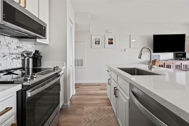 kitchen with light wood finished floors, decorative backsplash, light stone counters, appliances with stainless steel finishes, and a sink