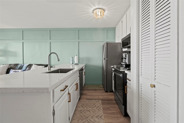 kitchen featuring a decorative wall, stainless steel appliances, a sink, white cabinets, and dark wood-style floors