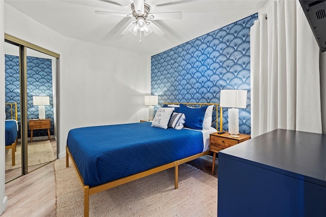 bedroom featuring an accent wall, light wood finished floors, a ceiling fan, and wallpapered walls