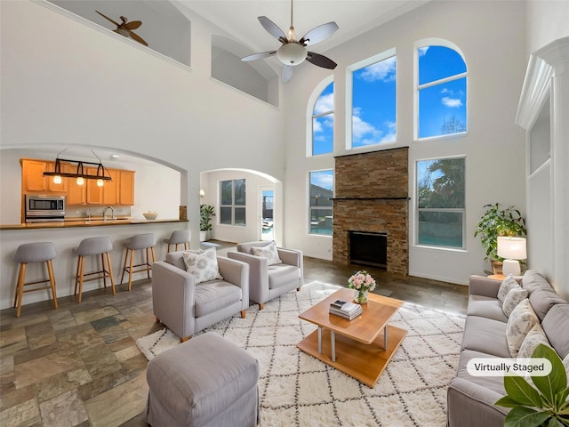 living room featuring stone finish flooring, baseboards, a ceiling fan, and a stone fireplace