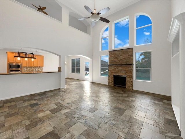 unfurnished living room with a ceiling fan, baseboards, a sink, and stone tile floors