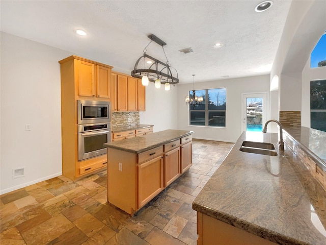 kitchen featuring stone tile floors, stainless steel appliances, tasteful backsplash, an inviting chandelier, and a sink