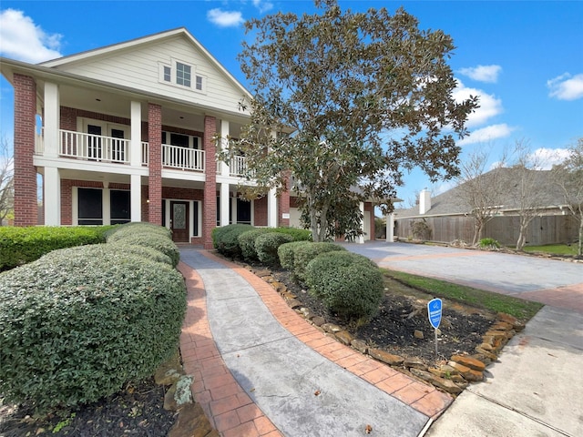 greek revival house featuring brick siding, driveway, a balcony, and fence